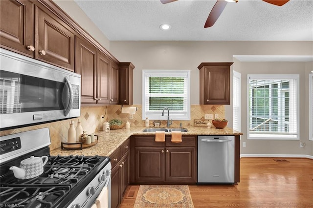 kitchen with stainless steel appliances, a ceiling fan, a sink, light wood-style floors, and light stone counters