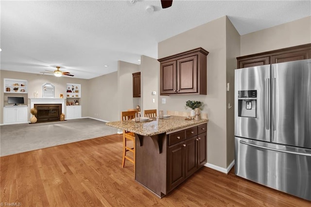 kitchen featuring stainless steel fridge with ice dispenser, a ceiling fan, a breakfast bar area, a peninsula, and a textured ceiling
