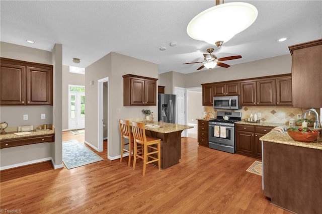 kitchen featuring stainless steel appliances, backsplash, light wood-type flooring, a breakfast bar area, and ceiling fan