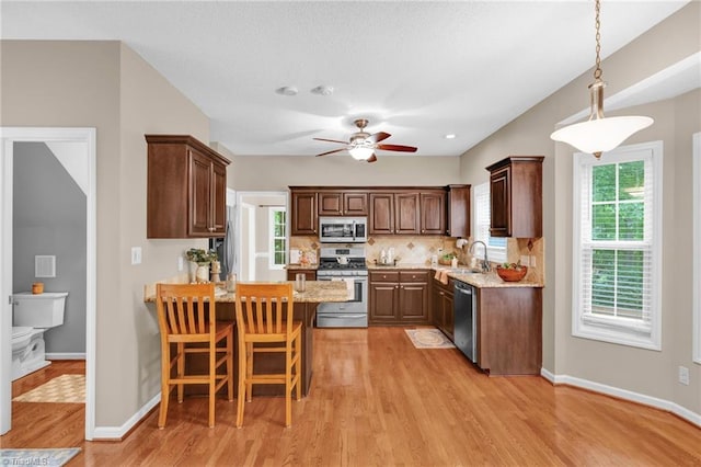 kitchen featuring appliances with stainless steel finishes, a peninsula, light wood-type flooring, ceiling fan, and decorative backsplash