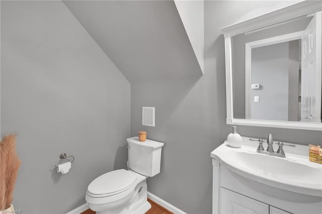 half bath featuring baseboards, toilet, vanity, and vaulted ceiling