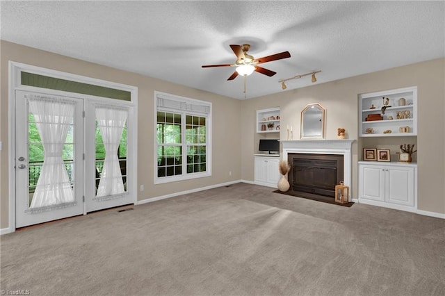 unfurnished living room with a fireplace with flush hearth, carpet floors, ceiling fan, a textured ceiling, and baseboards