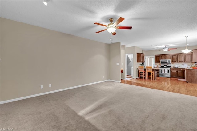 unfurnished living room featuring light carpet, ceiling fan, baseboards, and a textured ceiling