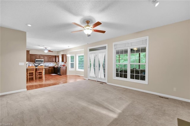 unfurnished living room with light colored carpet, ceiling fan, baseboards, and a textured ceiling