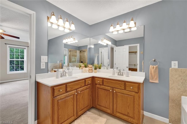 bathroom with a shower stall, double vanity, a ceiling fan, a textured ceiling, and baseboards