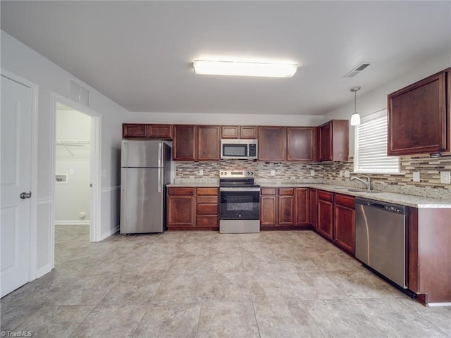 kitchen featuring appliances with stainless steel finishes, backsplash, light stone counters, sink, and pendant lighting