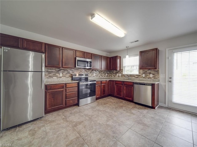 kitchen featuring pendant lighting, stainless steel appliances, light stone counters, and a wealth of natural light