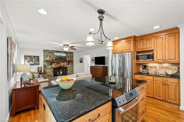 5017 Timbrook Ln, Winston-Salem, NC 27103 - kitchen featuring appliances with stainless steel finishes, a stone fireplace, ceiling fan, light wood-type flooring, and backsplash