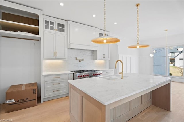 kitchen featuring double oven range, decorative light fixtures, white cabinets, and an island with sink