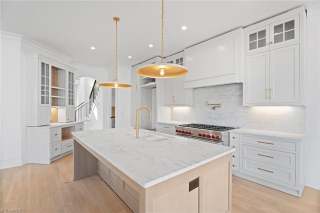 kitchen featuring light stone counters, hanging light fixtures, high end stainless steel range oven, a kitchen island with sink, and white cabinets