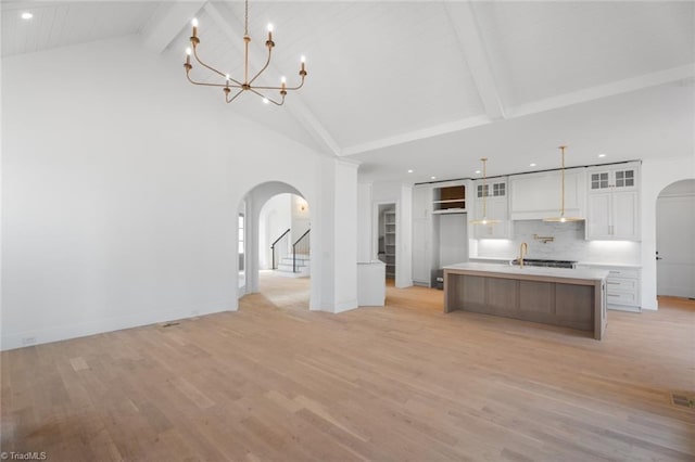 unfurnished living room with light hardwood / wood-style flooring, pendant lighting, a large island, white cabinets, and beam ceiling