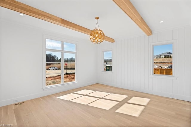 empty room with beamed ceiling, light wood-type flooring, and a wealth of natural light