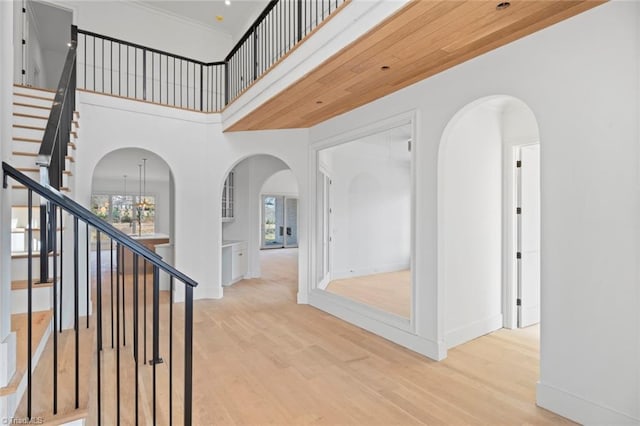 corridor featuring an inviting chandelier, a towering ceiling, light hardwood / wood-style flooring, and a healthy amount of sunlight