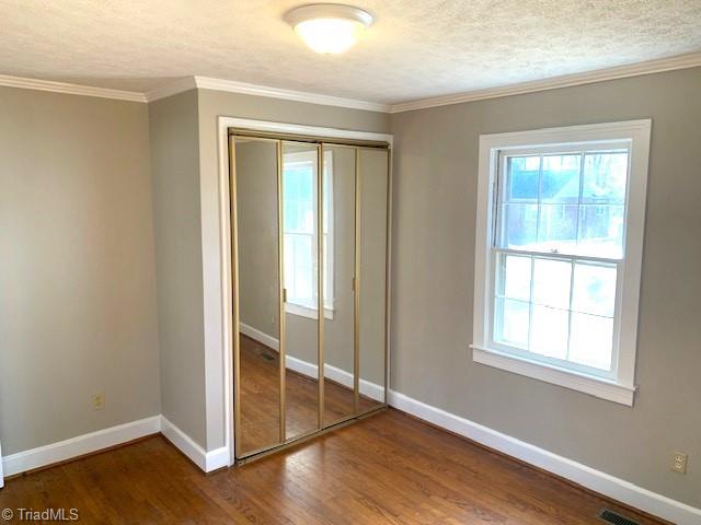 unfurnished bedroom featuring crown molding, a closet, a textured ceiling, and hardwood / wood-style flooring