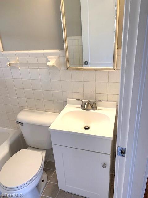 bathroom featuring vanity, a bath, tile patterned flooring, toilet, and tile walls