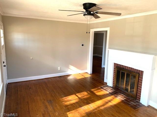 unfurnished living room featuring crown molding, ceiling fan, a fireplace, and dark wood-type flooring