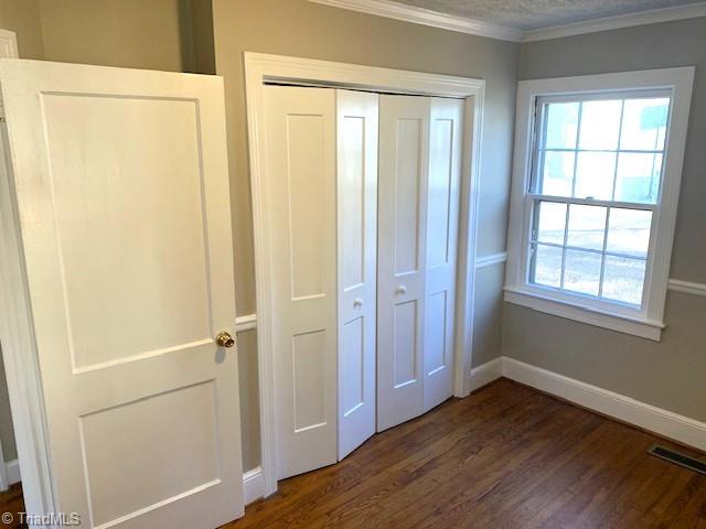 unfurnished bedroom with a textured ceiling, dark hardwood / wood-style flooring, a closet, and ornamental molding