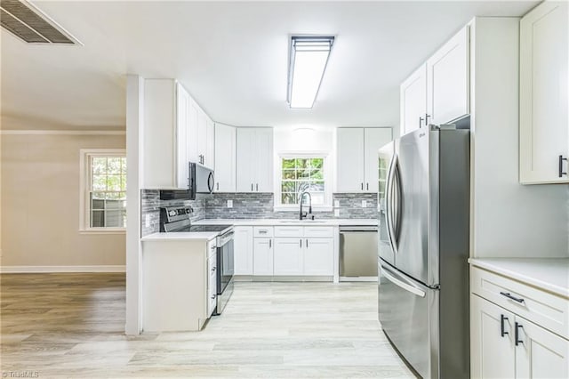 kitchen featuring appliances with stainless steel finishes, a sink, backsplash, and light wood finished floors