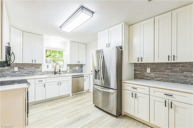 kitchen featuring appliances with stainless steel finishes, a sink, tasteful backsplash, light countertops, and light wood-type flooring