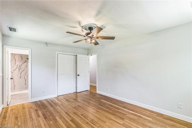 unfurnished bedroom with baseboards, light wood-style floors, a closet, ensuite bathroom, and a textured ceiling