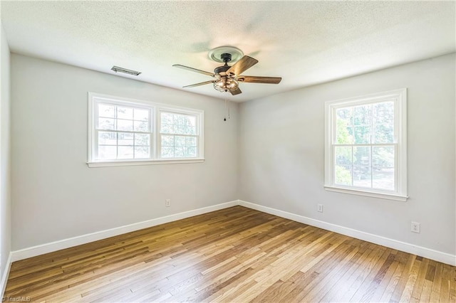 empty room featuring healthy amount of natural light, ceiling fan, hardwood / wood-style floors, baseboards, and a textured ceiling