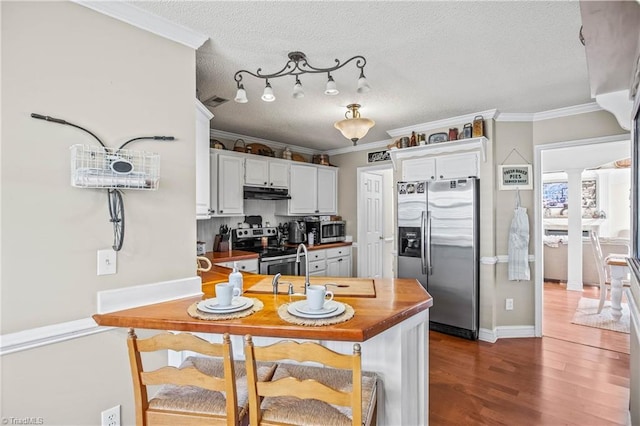 kitchen featuring butcher block countertops, white cabinets, ornamental molding, stainless steel appliances, and a textured ceiling