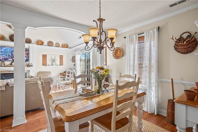 dining space featuring decorative columns, ornamental molding, a notable chandelier, a textured ceiling, and light hardwood / wood-style flooring