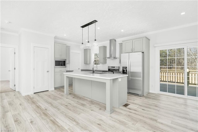 kitchen featuring appliances with stainless steel finishes, sink, gray cabinetry, a kitchen island with sink, and wall chimney exhaust hood