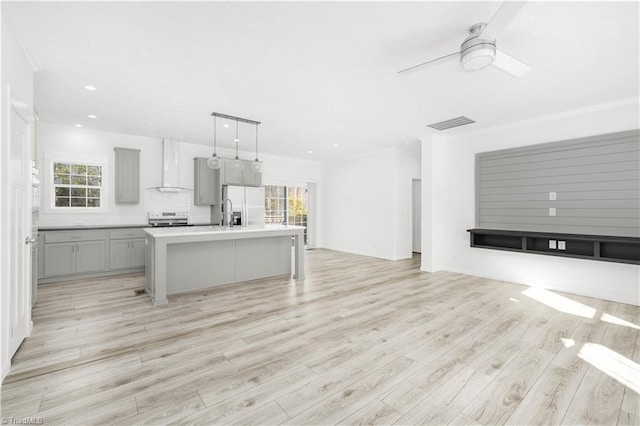 kitchen featuring pendant lighting, gray cabinets, plenty of natural light, stainless steel refrigerator with ice dispenser, and an island with sink