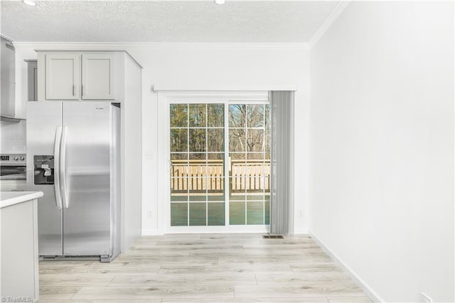 kitchen featuring gray cabinetry, crown molding, a textured ceiling, light wood-type flooring, and stainless steel fridge