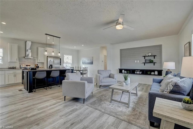 living room featuring ceiling fan, a textured ceiling, and light wood-type flooring