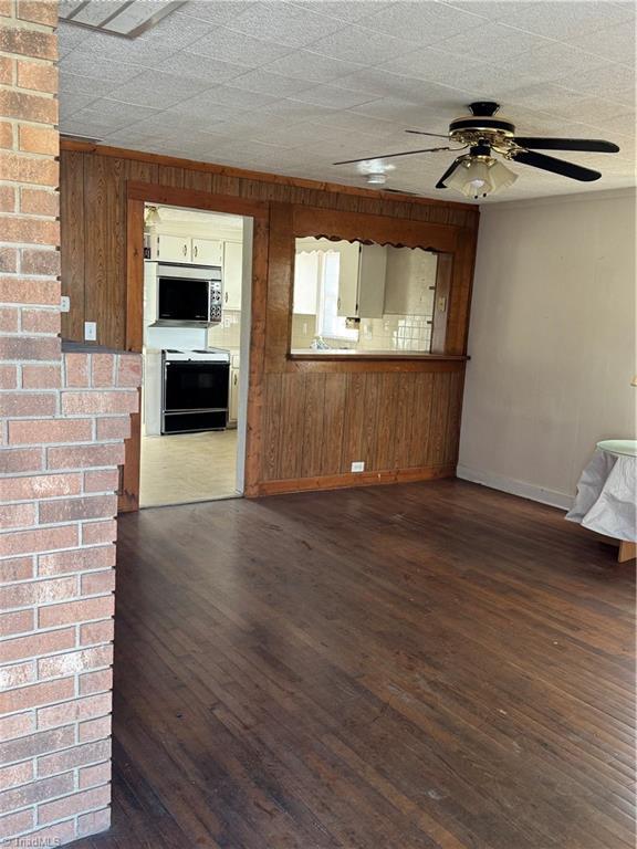 unfurnished living room with ceiling fan, wood walls, and dark hardwood / wood-style flooring