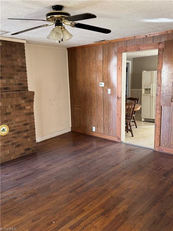 unfurnished room with ceiling fan, dark wood-type flooring, a textured ceiling, wooden walls, and ornamental molding