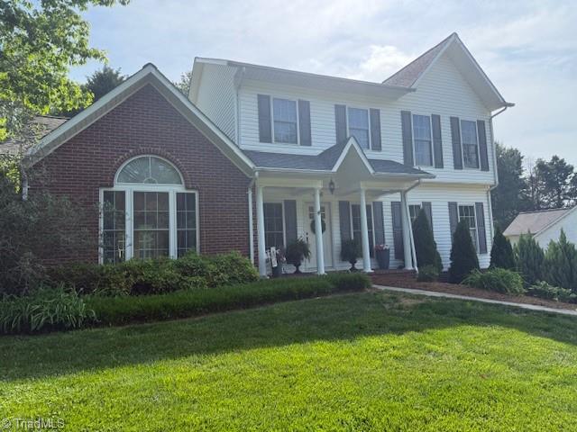 traditional-style house with a porch, a front yard, and brick siding