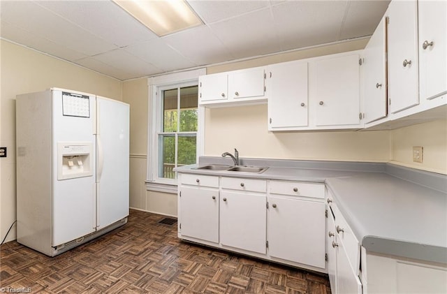 kitchen with dark parquet flooring, sink, white refrigerator with ice dispenser, and white cabinets