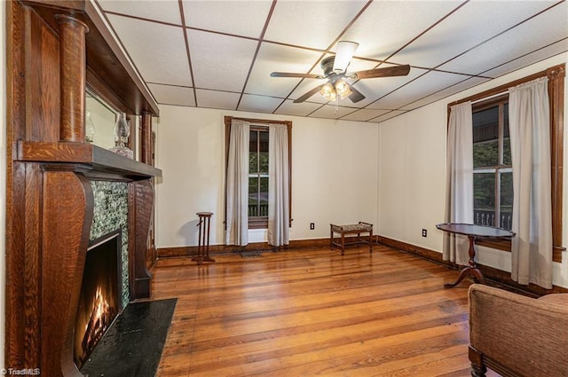 living area featuring ceiling fan, a fireplace, a paneled ceiling, and hardwood / wood-style floors