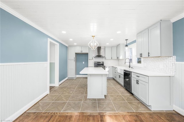 kitchen featuring a wainscoted wall, wall chimney exhaust hood, a kitchen island, appliances with stainless steel finishes, and light countertops