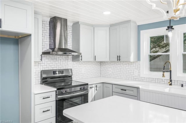 kitchen with decorative backsplash, light countertops, electric range, and wall chimney exhaust hood