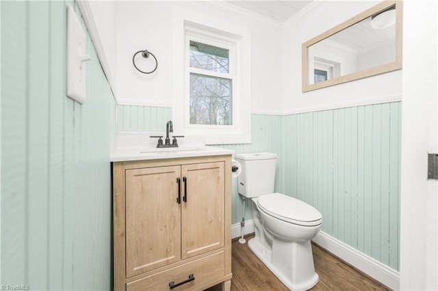 bathroom featuring toilet, wood finished floors, vanity, wainscoting, and crown molding