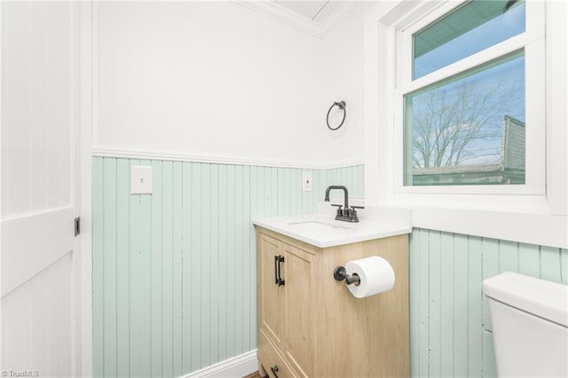 half bath featuring wainscoting, vanity, toilet, and crown molding