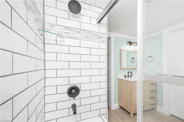 full bath featuring wood tiled floor, a tile shower, crown molding, and vanity