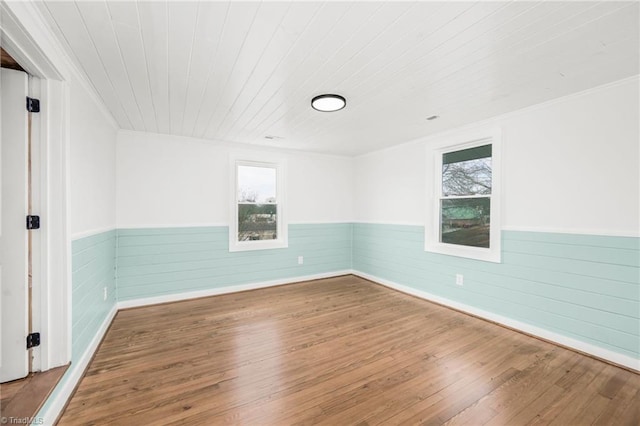 unfurnished room with wood-type flooring, a wainscoted wall, and plenty of natural light