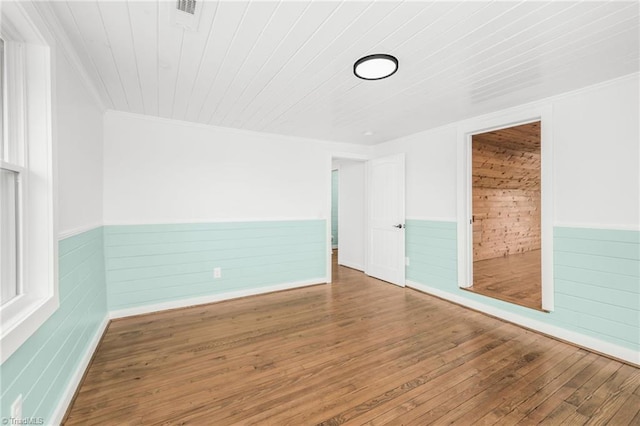 spare room with a wainscoted wall, ornamental molding, wood-type flooring, and wood ceiling