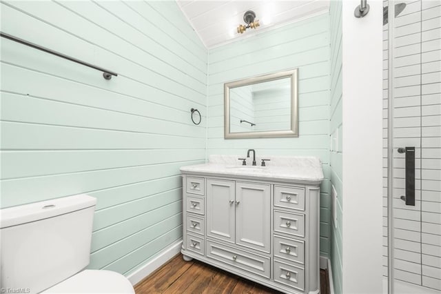 bathroom featuring toilet, vaulted ceiling, wooden walls, vanity, and wood finished floors