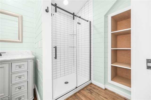 full bathroom with a stall shower, wooden walls, vanity, and wood finished floors