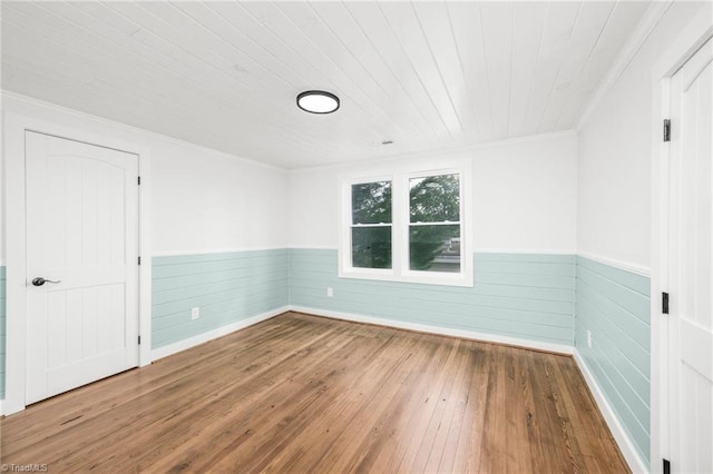 empty room with wainscoting, wood-type flooring, wood ceiling, and crown molding