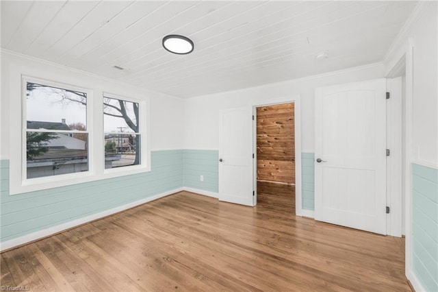 empty room featuring a wainscoted wall, ornamental molding, and wood finished floors