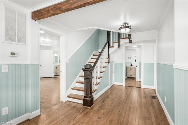 foyer entrance featuring stairs, a wainscoted wall, wood-type flooring, and beam ceiling