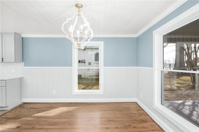 unfurnished dining area with a chandelier, wainscoting, crown molding, and wood finished floors