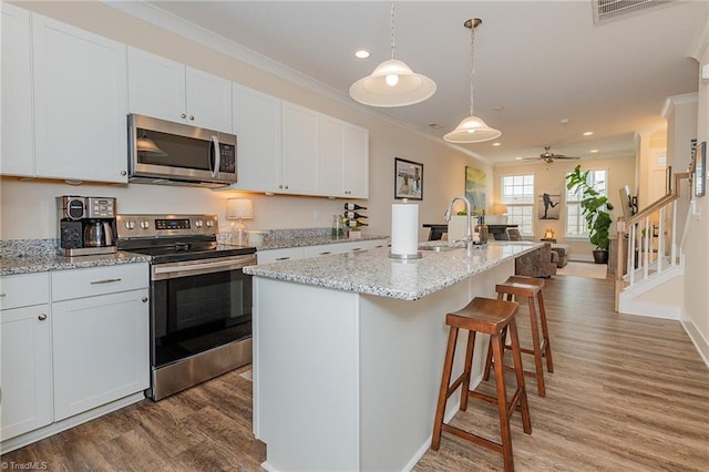 kitchen featuring visible vents, light wood-style floors, appliances with stainless steel finishes, a kitchen bar, and crown molding